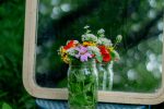 A rustic floral arrangement in a jar, reflected by a mirror, in a forest setting.